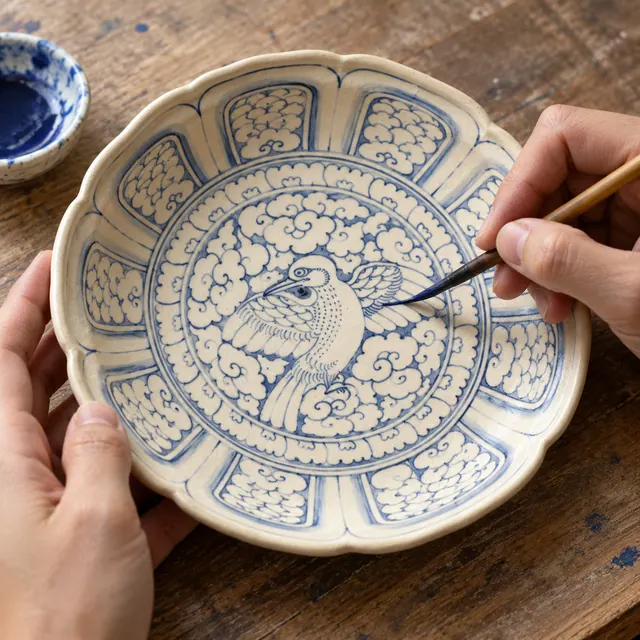 AI illustration: hands painting a bird-and-cloud design on a ceramic dish.